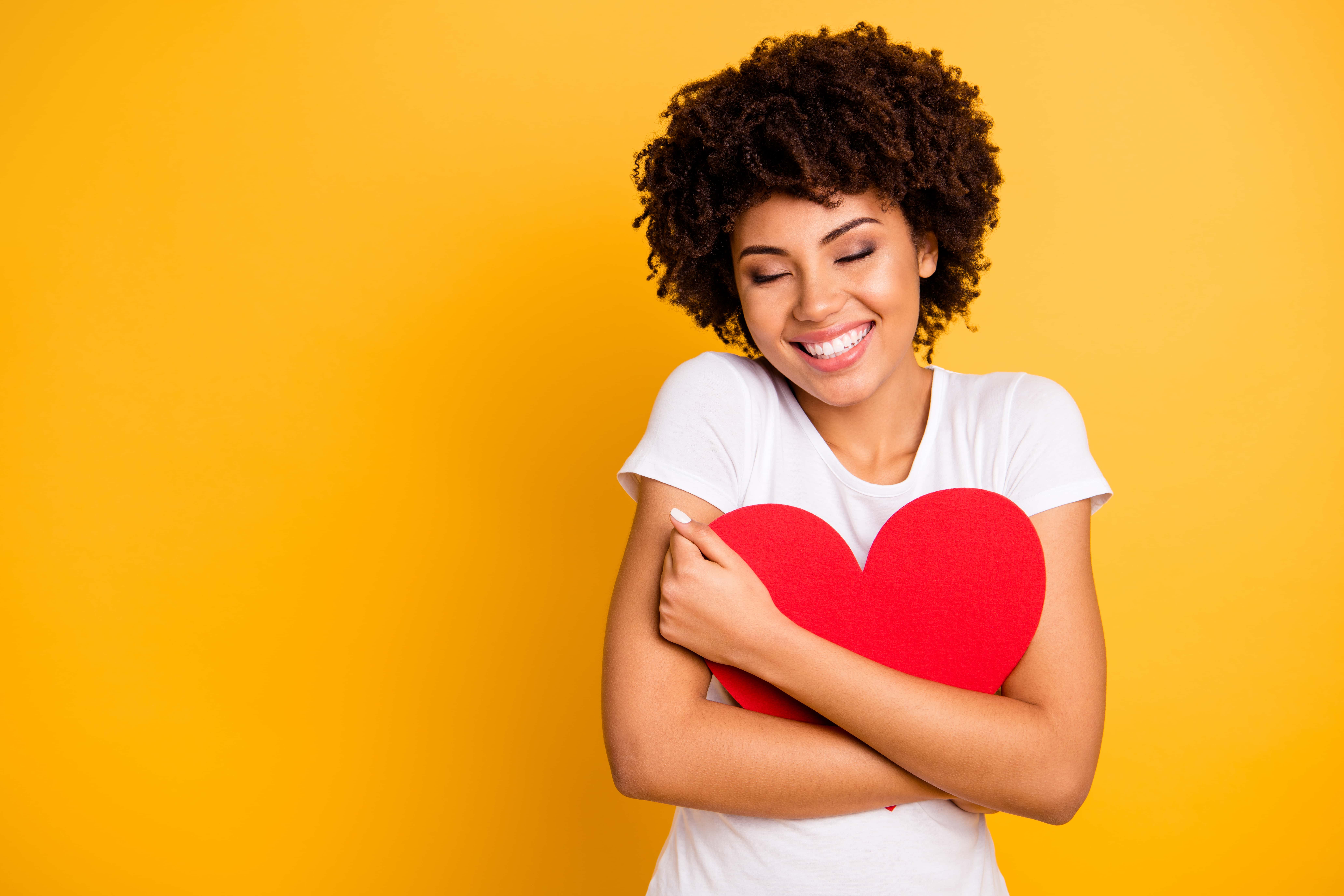 Attractive woman with curly brown hair in a white shirt cuddling big paper card heart shape figure