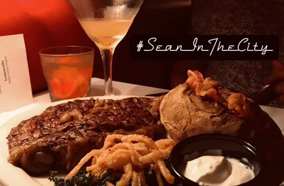 A steak, baked potato, and cocktail glass on a white plate.