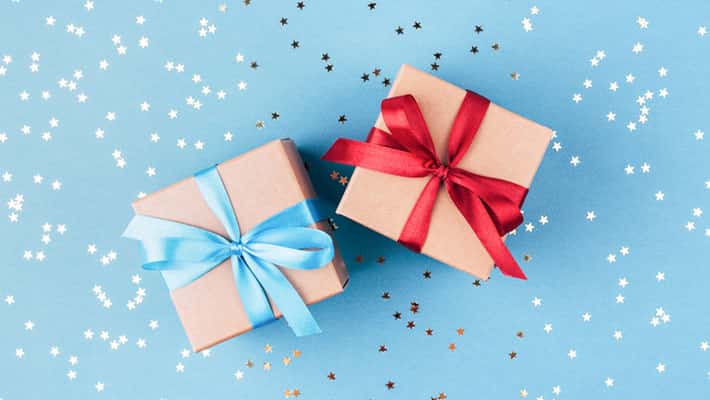 Two gift boxes wrapped in kraft paper and tied with ribbon on blue background decorated with confetti