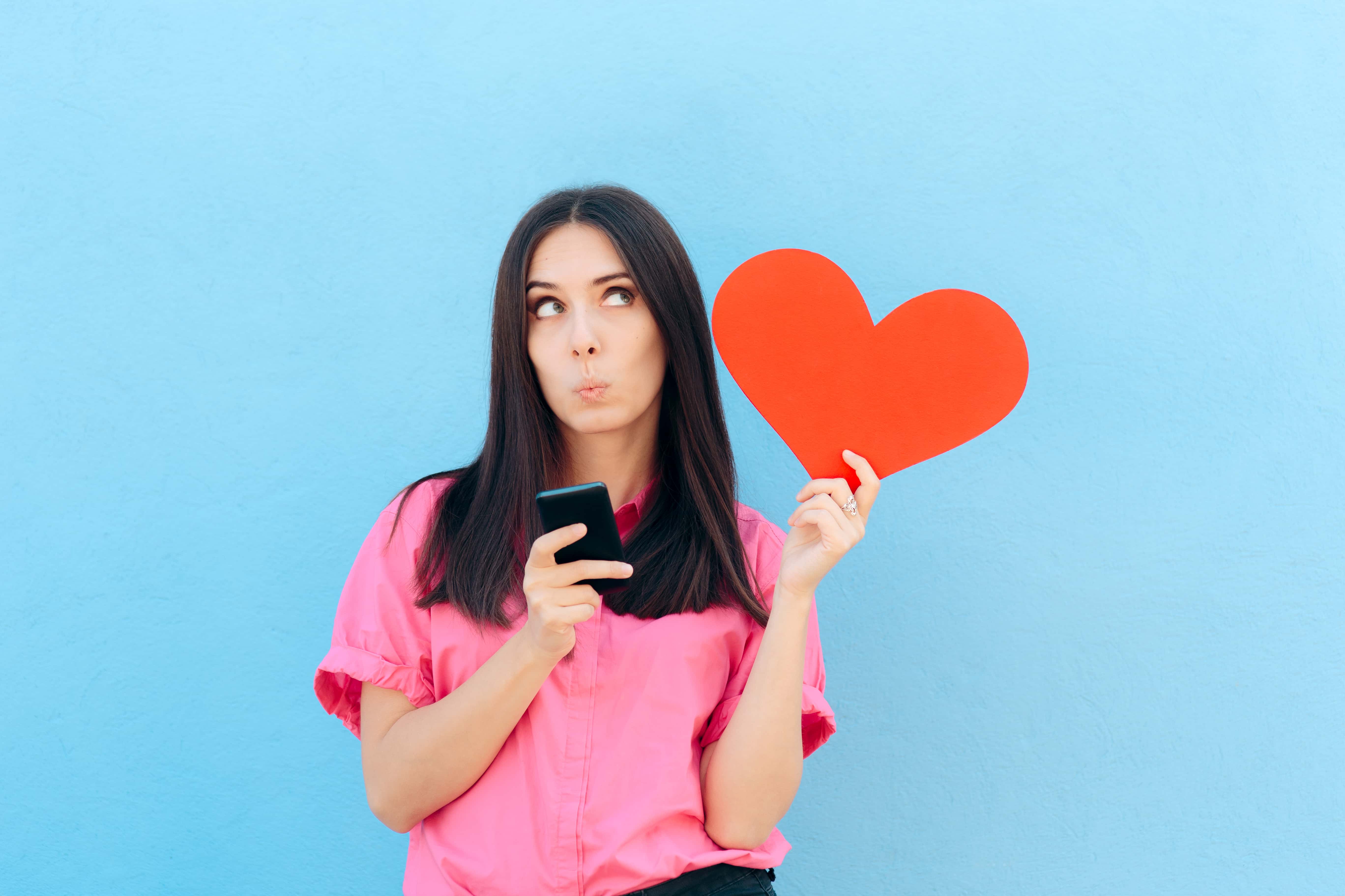 Girl using dating app on her phone while holding a red heart