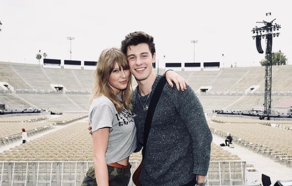 Taylor Swift and Shawn Mendez posing in front of empty chairs on stage