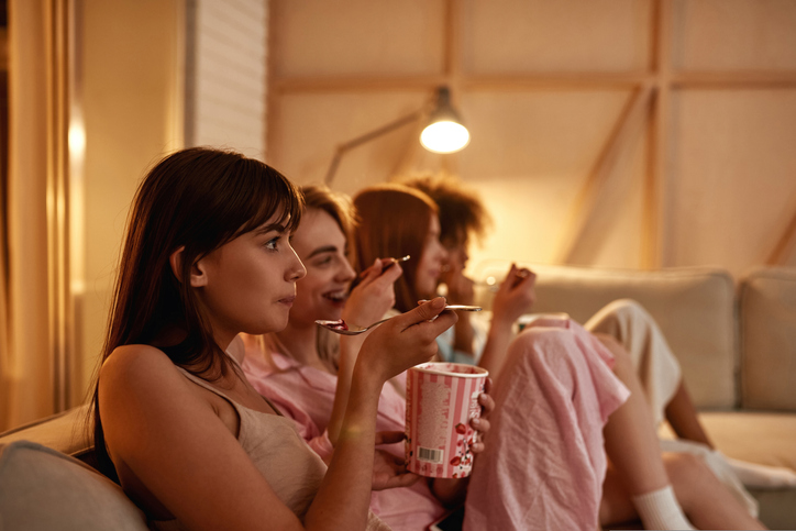 Young girlfriends eating ice cream and watching TV