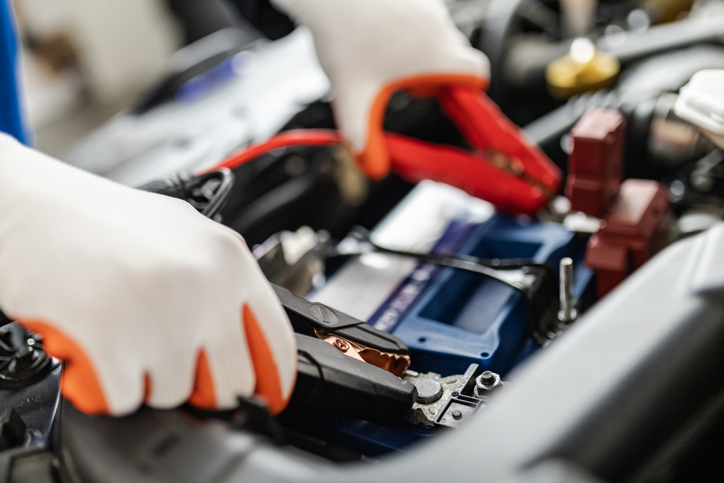 A mechanic connects jumper cables to a car battery in a garage during daytime, ensuring proper vehicle electrical function and troubleshooting issues