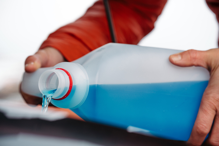 Pouring winter washer fluid into car reservoir during winter, protecting it from freezing.