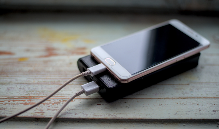 Powerbank charge smartphone on wooden table.