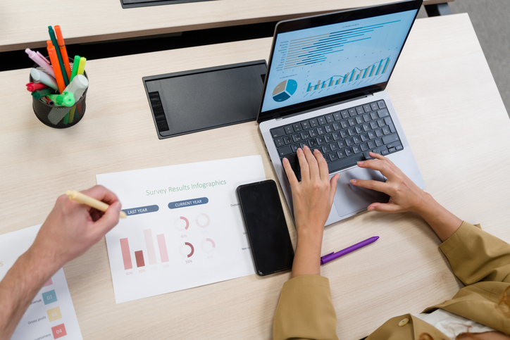 Business colleagues analyzing survey results infographics on laptop and paper