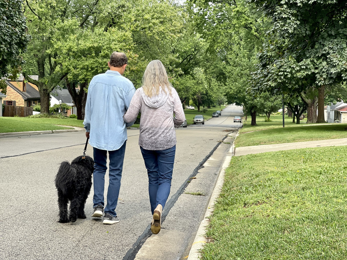 Active senior couple walking their Portuguese water dog in tree lined neighborhood. Rear view