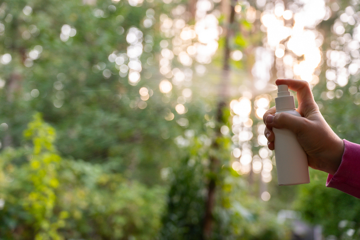 Person spraying insect repellent at her hand outdoors during summer