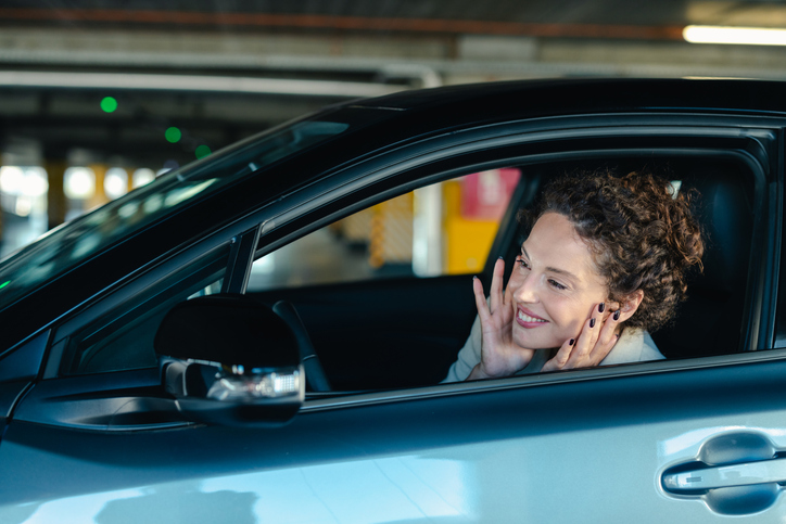 Smiling woman checking appearance in car's side mirror in parking garage