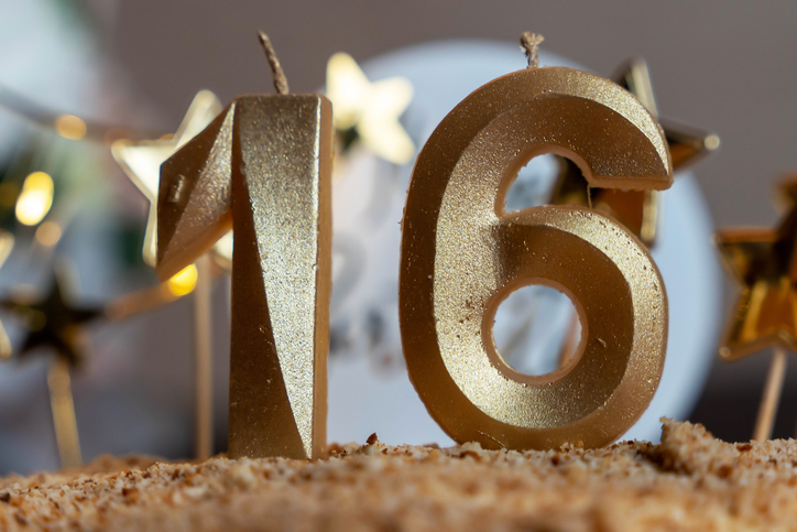 Golden sixteen birthday candles burning on cake with star decorations